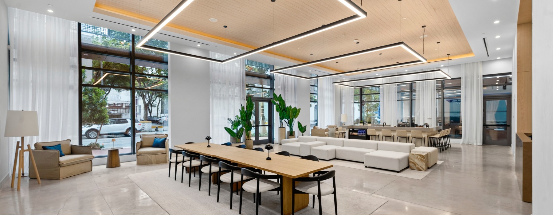 Modern lobby lounge at CMPND Miami with a communal table, sofas, and a designer wood-slat ceiling