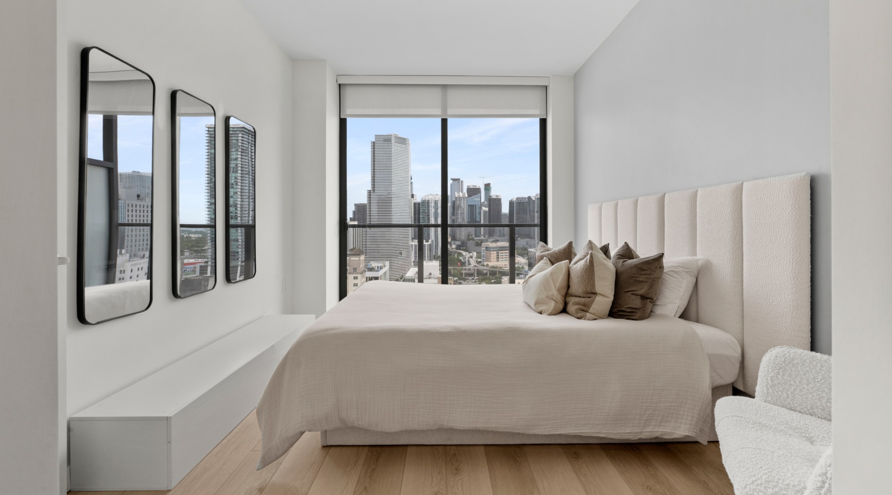 Bedroom in a luxury CMPND Miami apartment with upholstered headboard, wall mirrors, and floor-to-ceiling skyline views