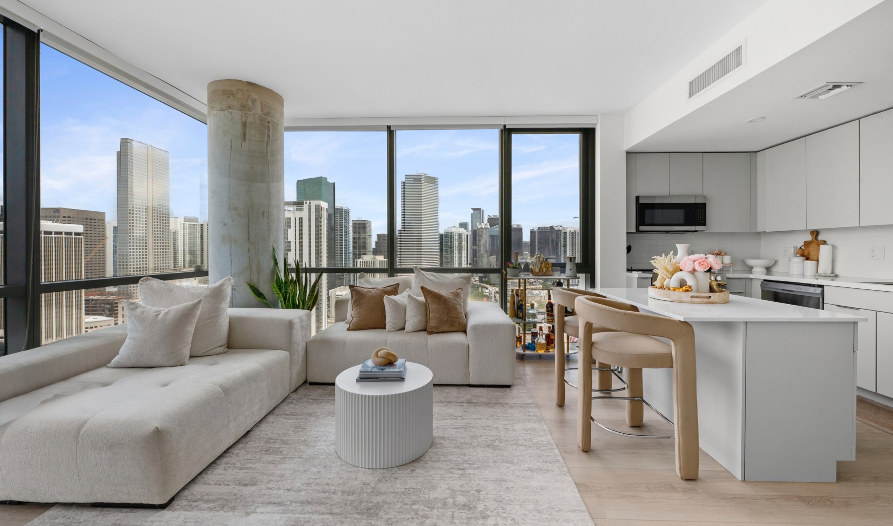 Bright living room and kitchen in a CMPND Miami apartment with wraparound windows and Miami skyline views